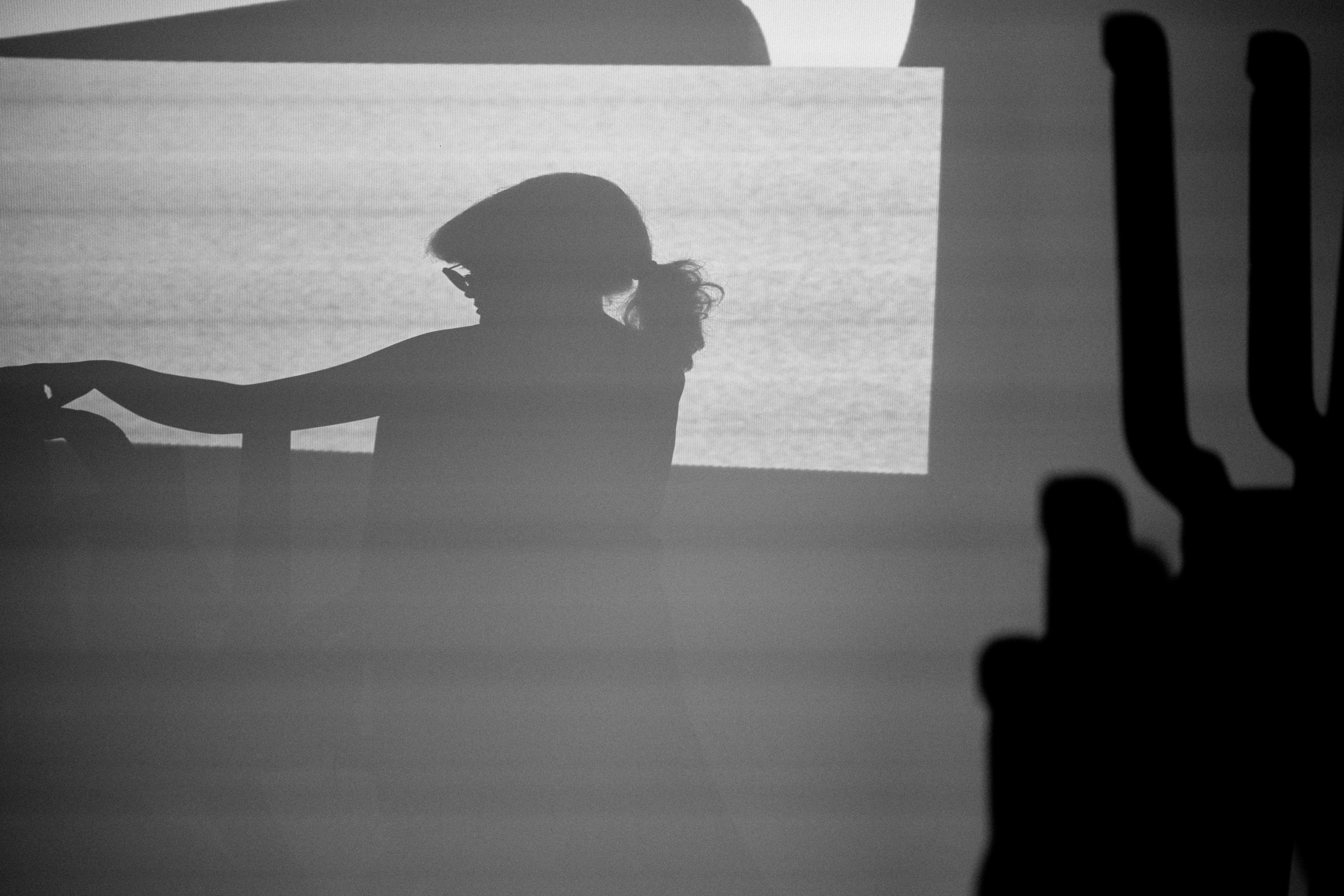 A black-and-white silhouette of a person with glasses and her hair tied back with a bright rectangular background.