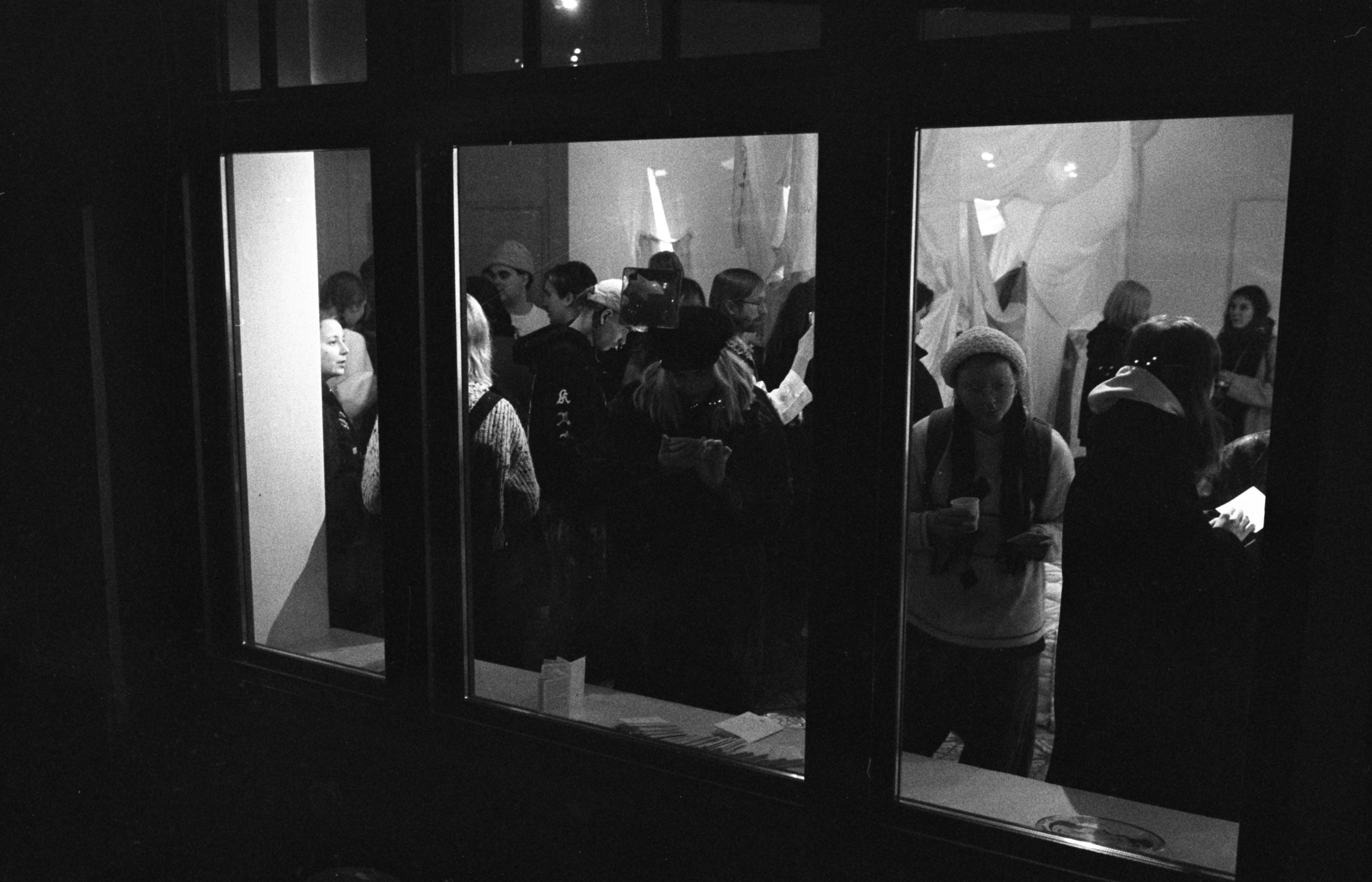 Kuva Maa-Tilan ikkunasta. Sisällä on käynnissä I have been waiting for awhile -näyttelyn avajaiset 10.1.2024.