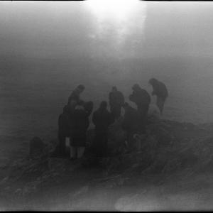 A dim photo of people huddled around each other on a rock by the sea.